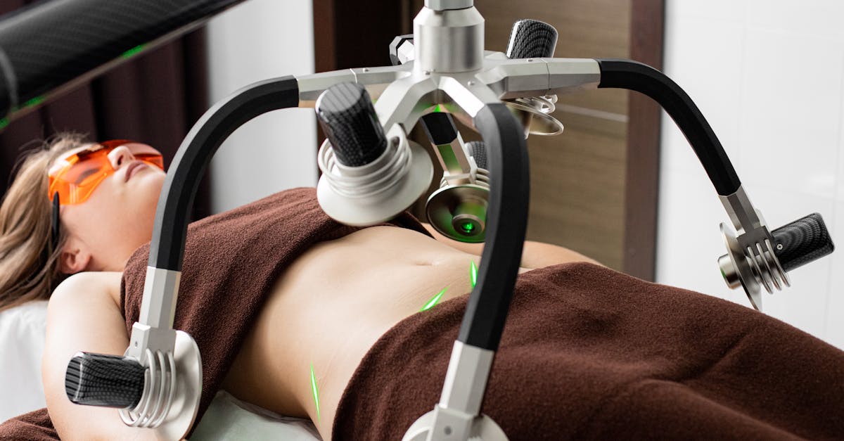 Female client lying on table under lasers of modern weight loss machine on belly during liposuction procedure in medical clinic